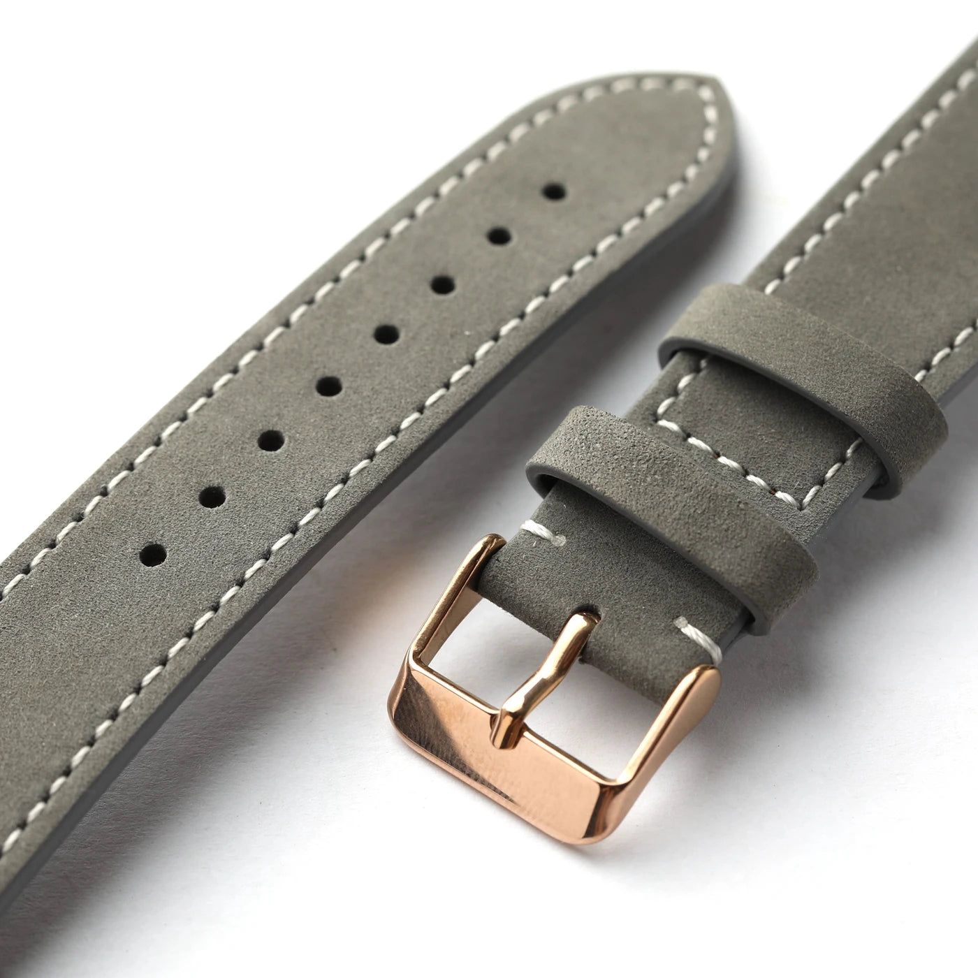 A close-up of a gray suede watch strap with white contrast stitching and a polished rose gold buckle, shown on a clean white background.