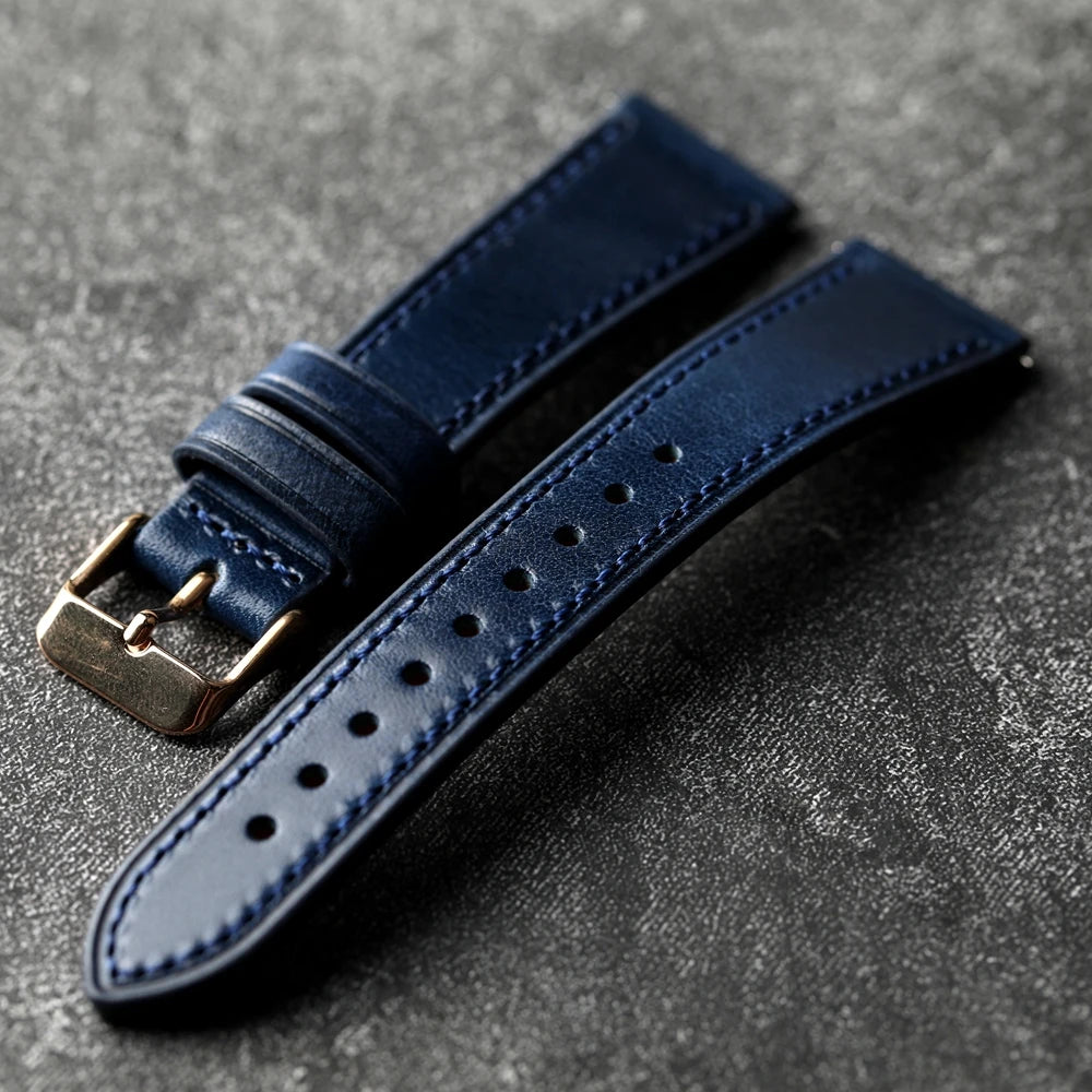 Blue leather watch strap with gold buckle on a gray surface
