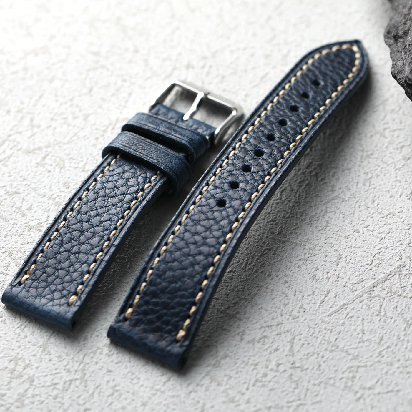 Blue leather watch strap with stitching on a light gray background