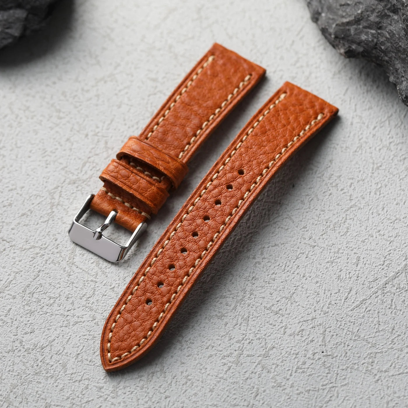 Brown leather watch strap with silver buckle on a gray surface