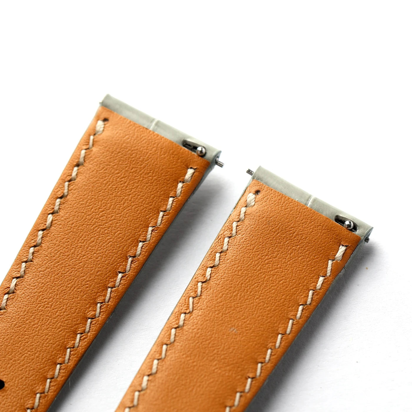 Close-up of a tan leather watch strap with white stitching and silver metal ends on a white background.