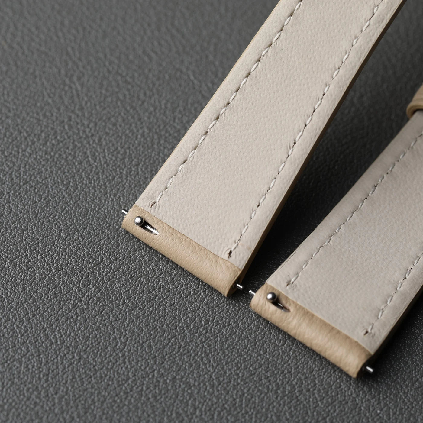 Close-up of beige leather straps with stitching on a gray background