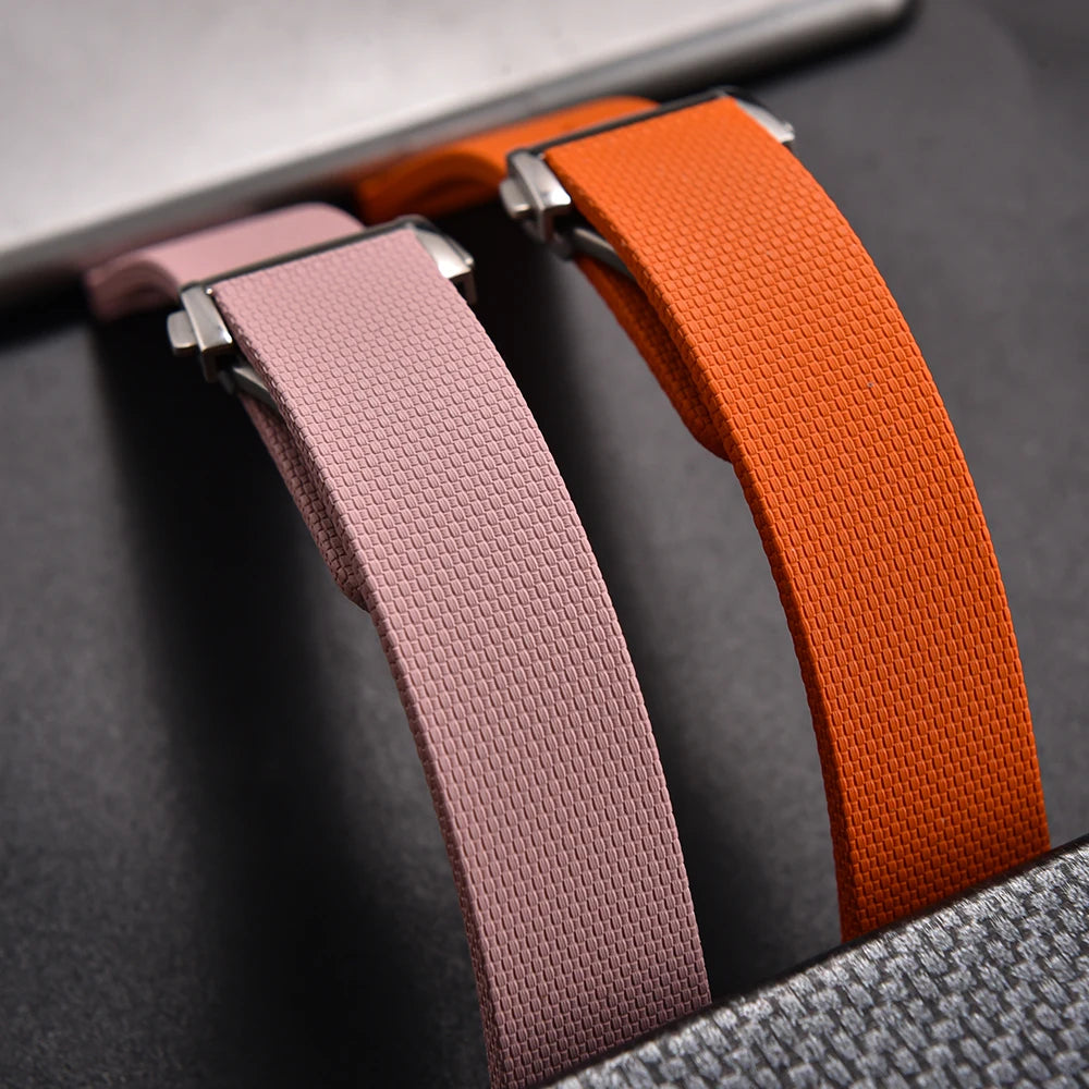 Close-up of three fabric straps in pink, orange, and gray on a textured surface.