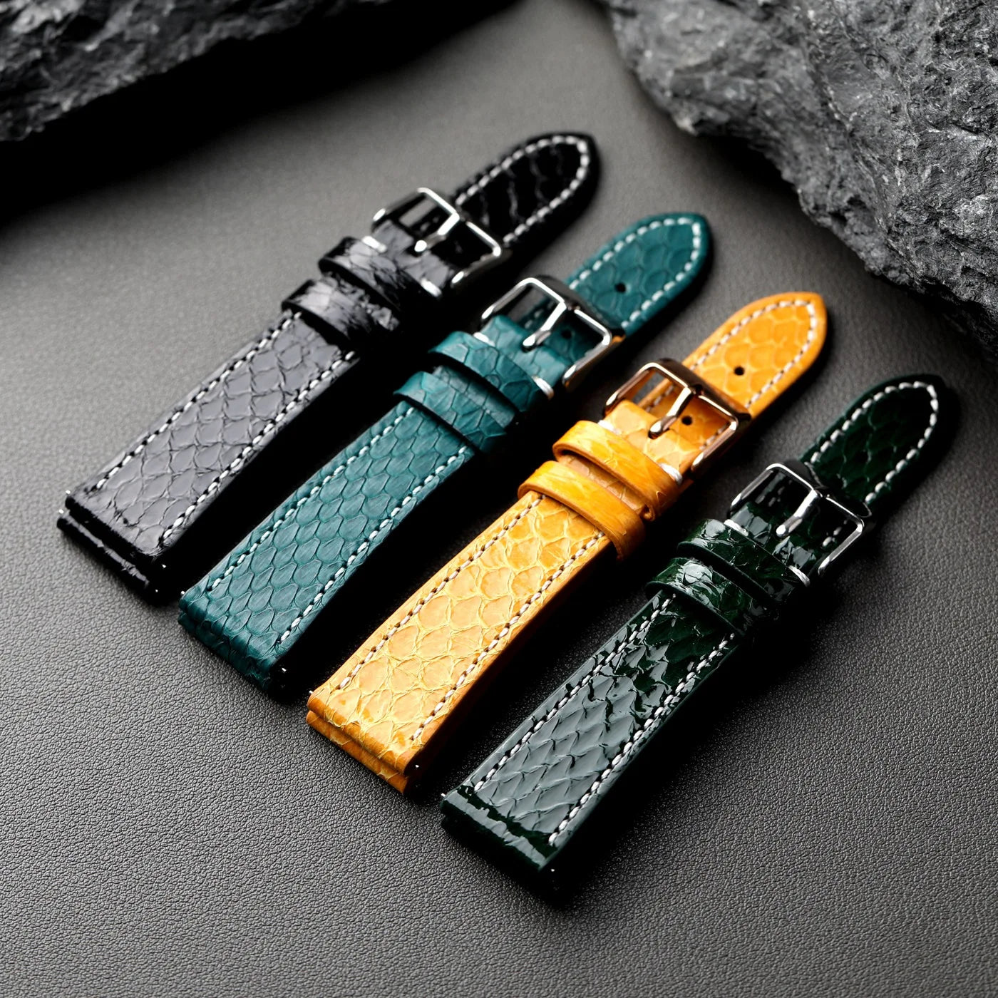 Python Snake Skin Four leather watch straps in black, green, yellow, and gray on a dark surface.