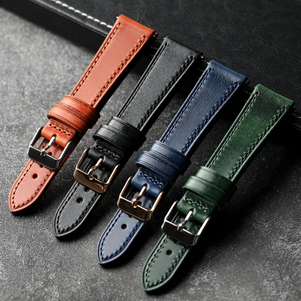 Four leather watch straps in brown, black, blue, and green on a dark surface.