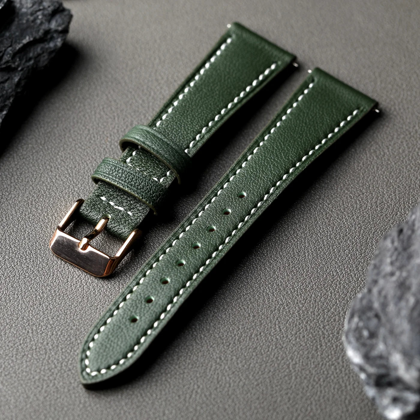 Green leather watch strap with rose gold buckle on a gray surface