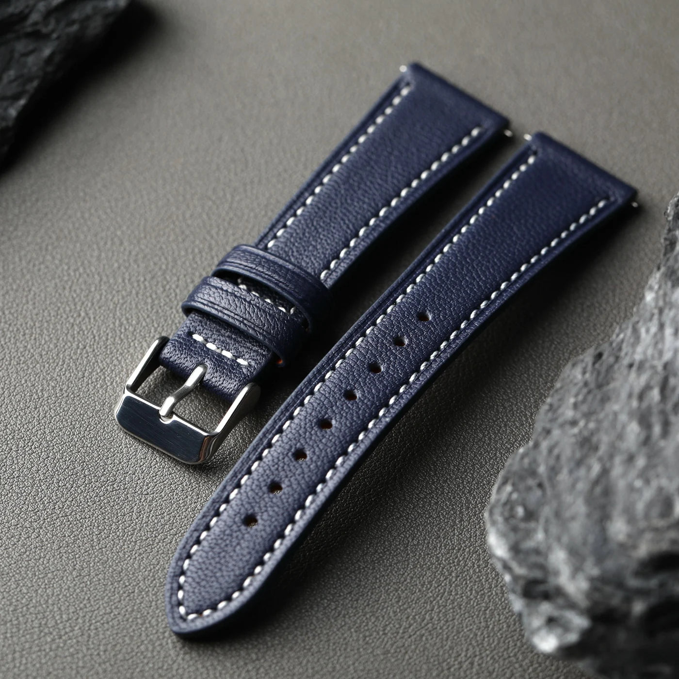 Navy blue leather watch strap with silver buckle on a gray surface
