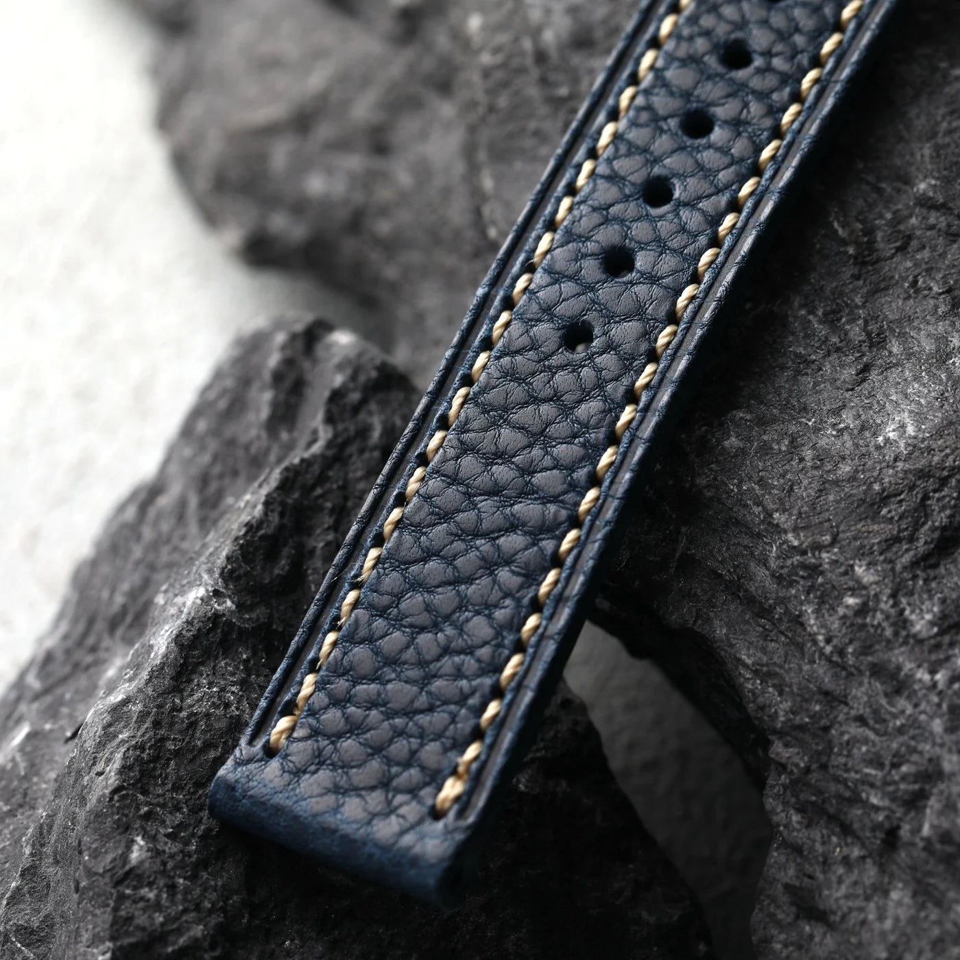 Navy leather strap with gold stitching on a stone surface