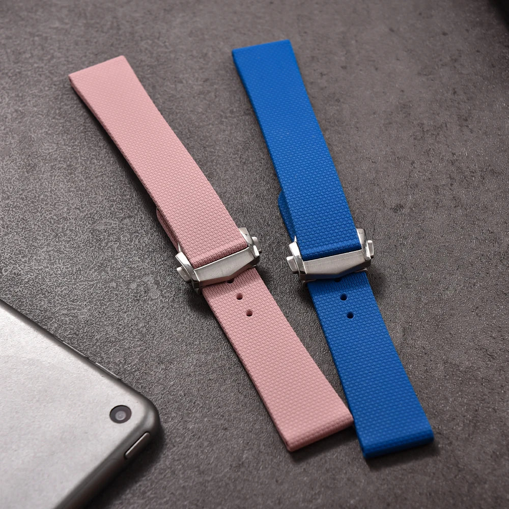 Pink and blue watch straps with silver buckles on a gray surface