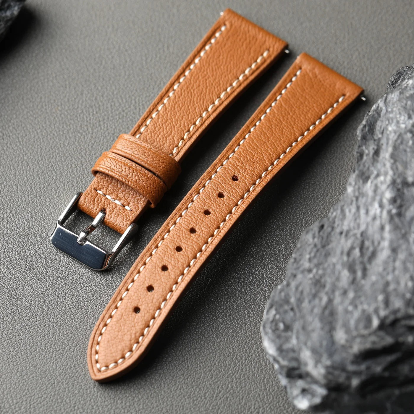 Brown leather watch strap with silver buckle on a gray surface