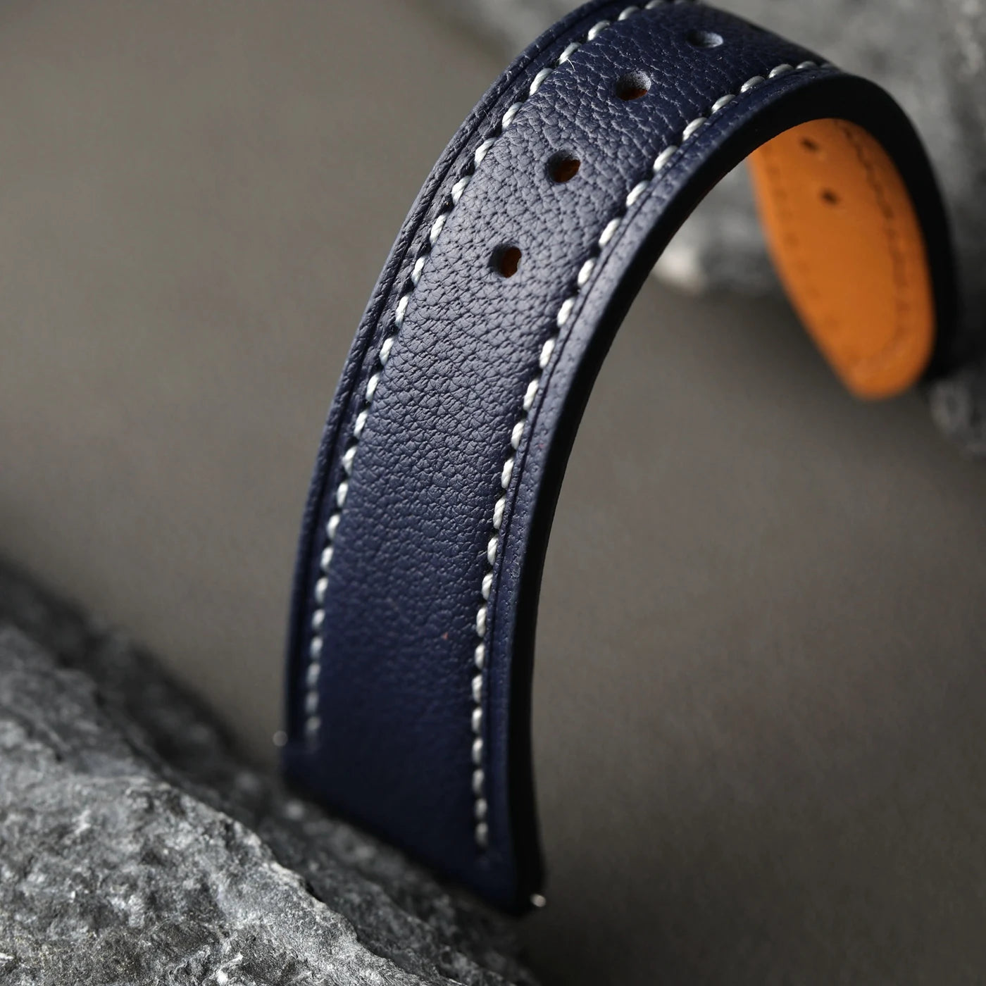 Close-up of a blue leather strap with white stitching on a gray background