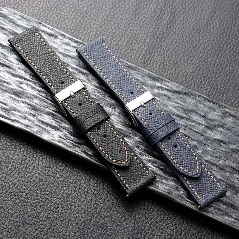 Two dark brown leather watch straps with silver buckles on a textured gray surface.