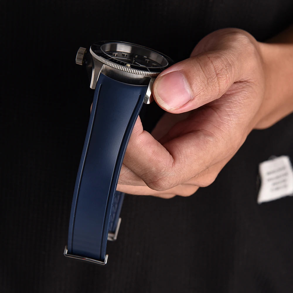 Hand holding a watch with a blue strap against a black background