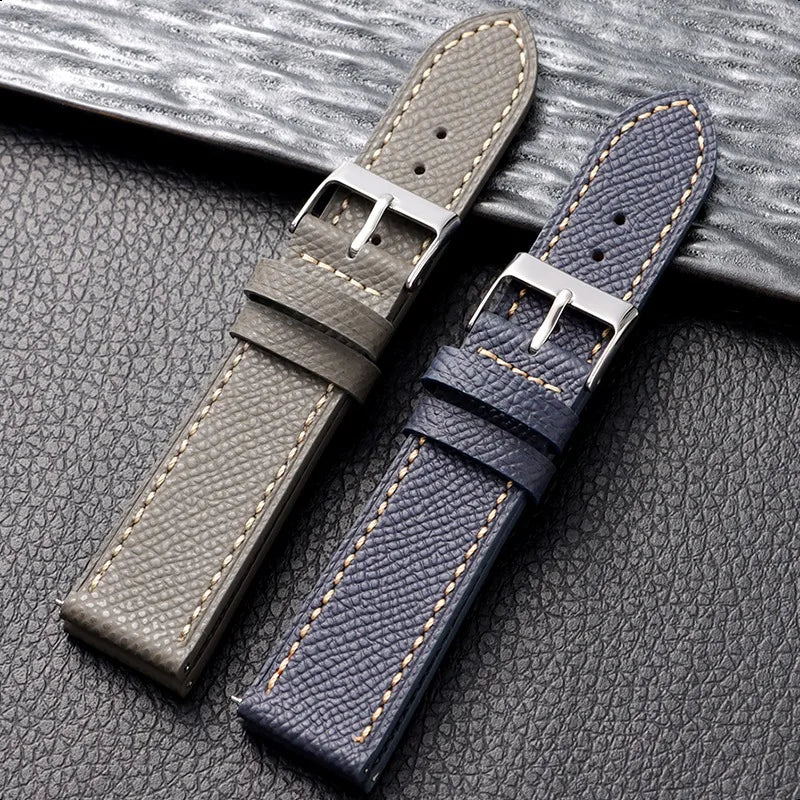 Two leather watch straps, one gray and one blue, on a textured surface.
