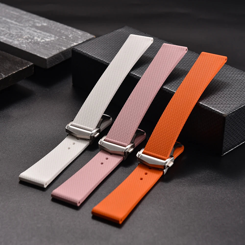 Three watch straps in white, pink, and orange on a dark surface