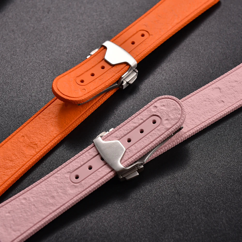 Two watch straps, one orange and one pink, with silver buckles on a dark background.